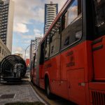 Ônibus vermelho parado em um ponto de transporte público no centro de Curitiba.
