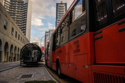 Ônibus vermelho parado em um ponto de transporte público no centro de Curitiba.
