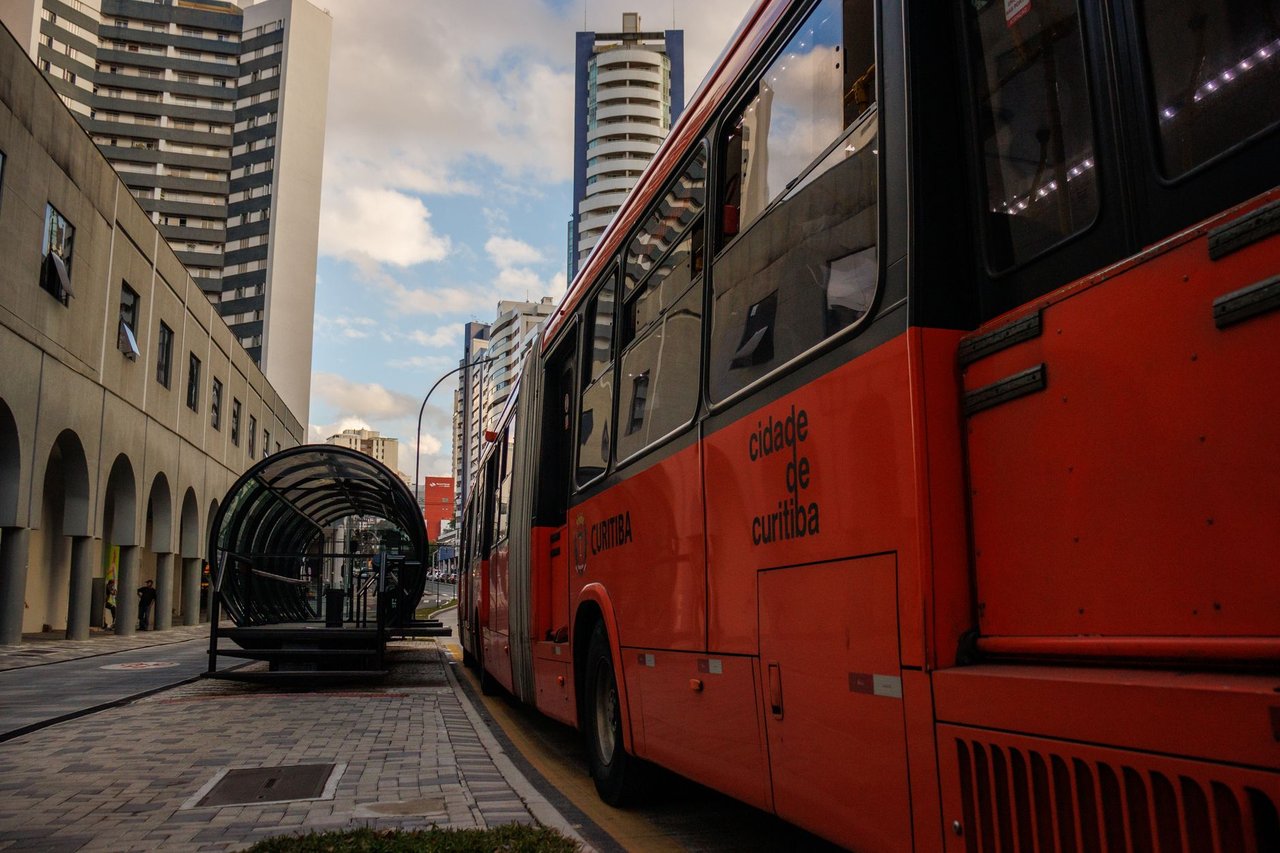 Ônibus vermelho parado em um ponto de transporte público no centro de Curitiba.