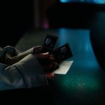 Pessoa segura ingressos de cinema durante a noite, em frente a uma entrada iluminada.