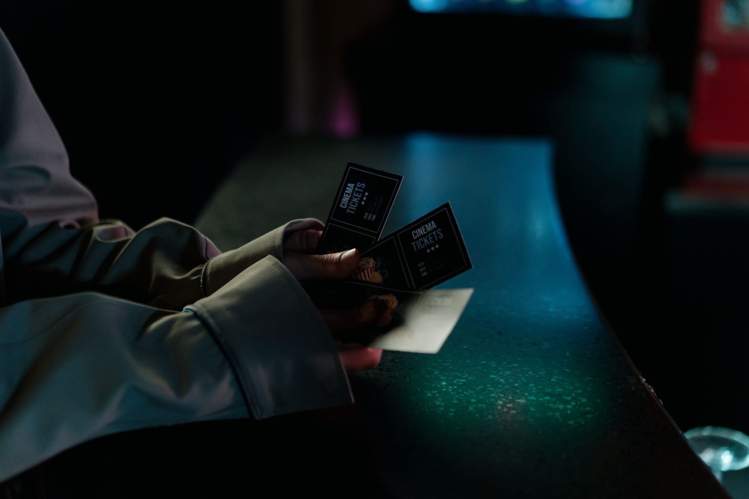 Pessoa segura ingressos de cinema durante a noite, em frente a uma entrada iluminada.